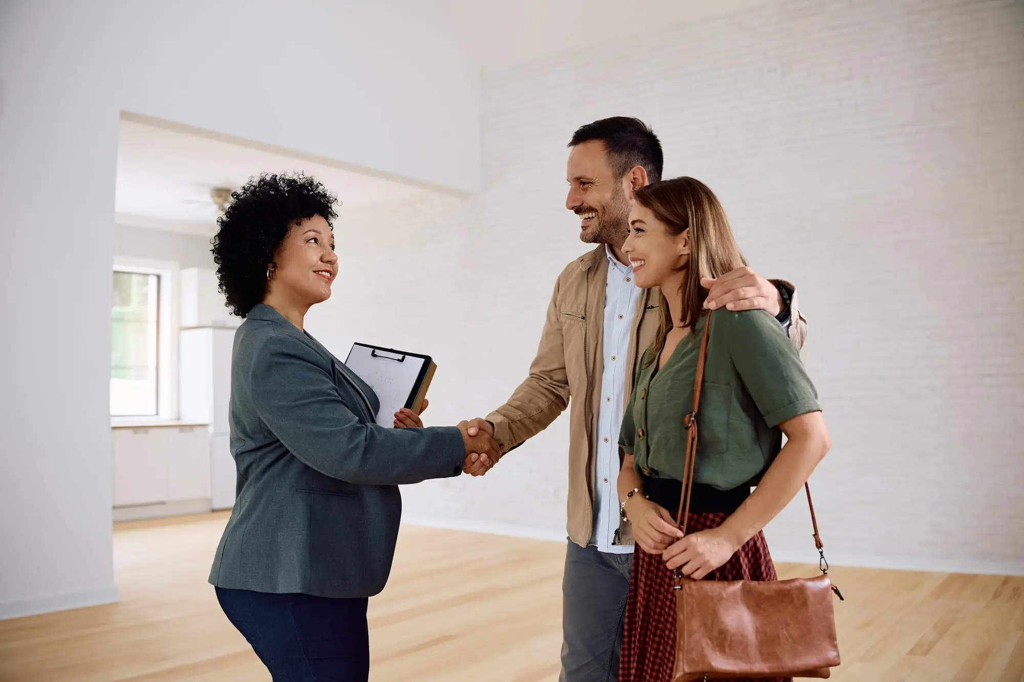 Happy couple and their real estate agent shaking hands in a new house.